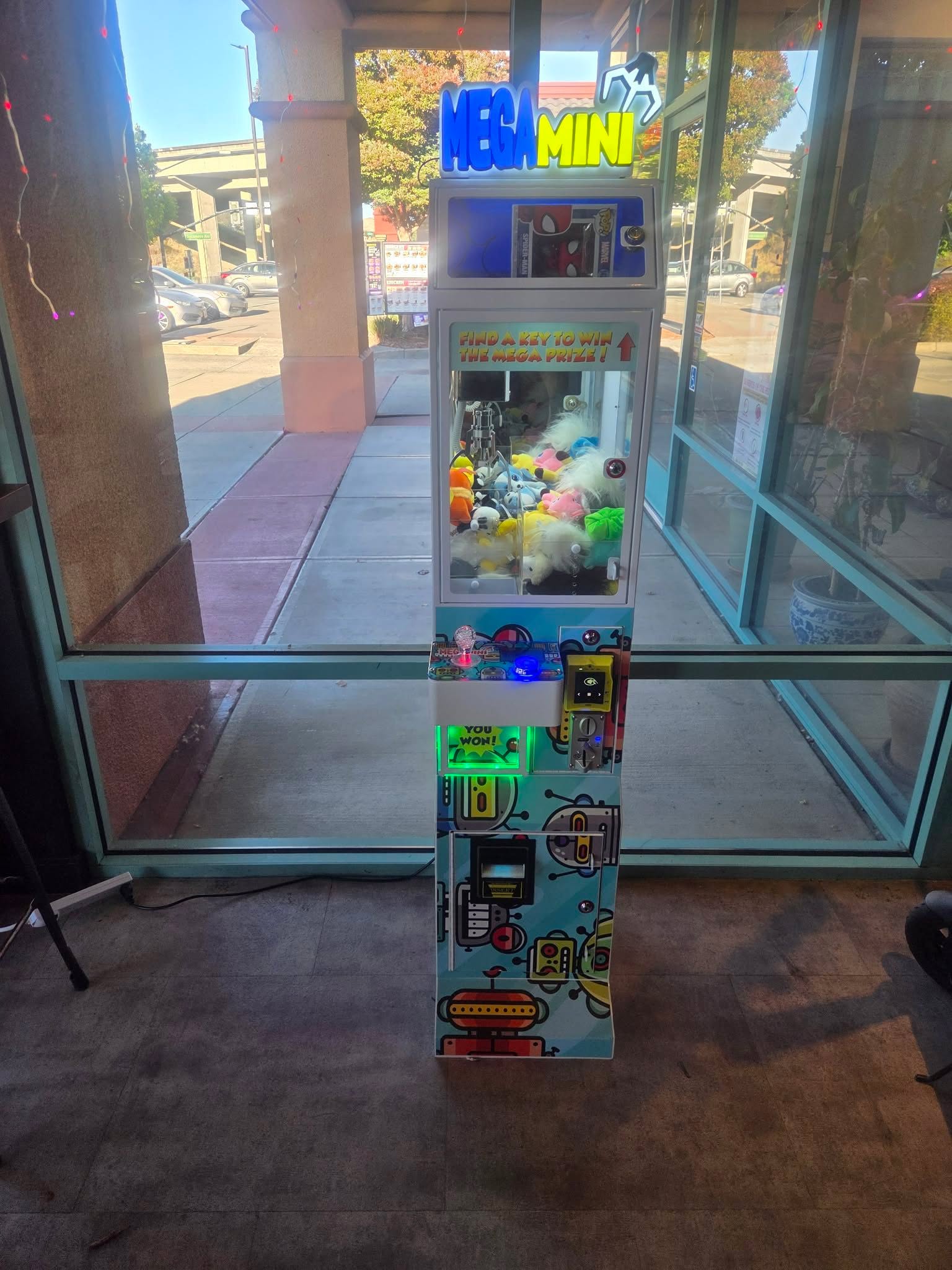 A lit-up DoBetter Mega Mini claw machine inside a storefront window